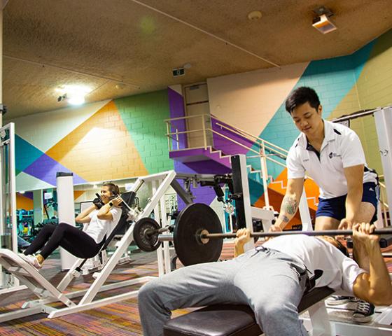 Decorative image - gym staff helping client bench press