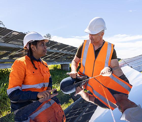 Man and woman wearing hi vis and hard hats working on solar panel